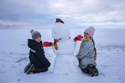 Happy boy and girl sit together with snowman. seasonal family weekend, active authentic lifestyle