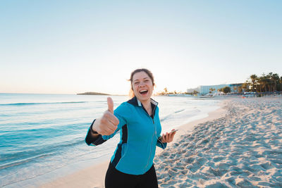 Smiling young man standing on beach against clear sky