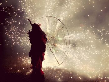 Silhouette man holding firework while standing on street at night