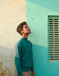 Young man looking away while standing by house