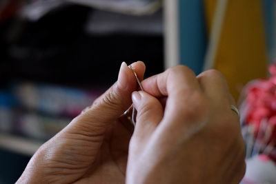 Cropped hand of woman inserting thread in needle