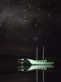 Sailboats moored on sea against sky at night