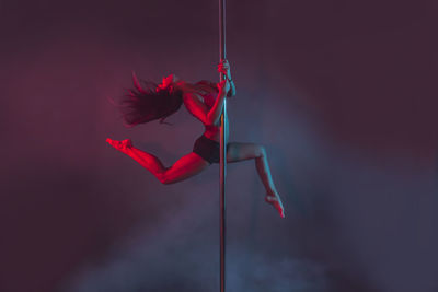 Young pole dancer performing against colored background
