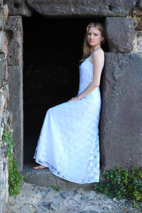 Sad young woman wearing white dress standing on doorway