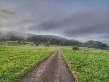 Empty road amidst field against sky