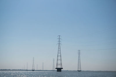 Electricity pylons on sea against clear sky