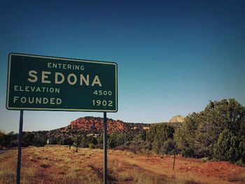 Road sign on landscape against clear blue sky