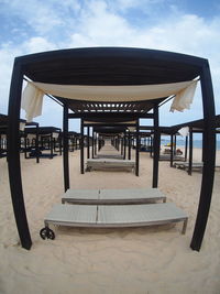 Empty benches on beach against sky