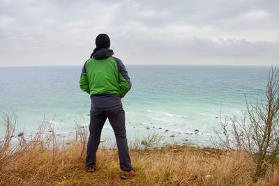 Tourist in green black clothing and cap with hands in the air along beach. vivid and vignetting 