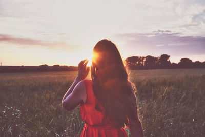 Rear view of woman standing by plants against sky during sunset