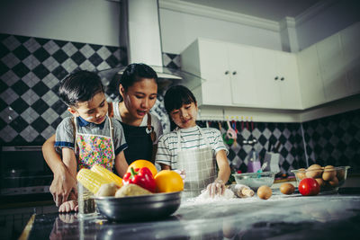 Mother with children kneading dough on kitchen counter while standing at home