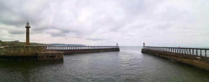 Bridge over sea against cloudy sky