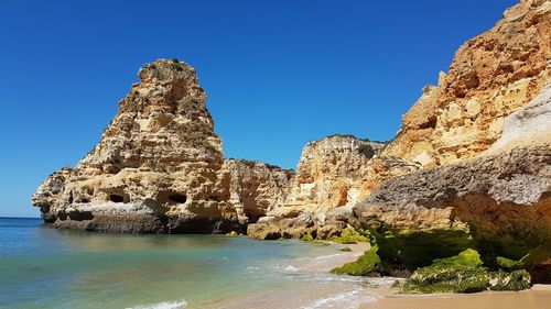 Rock formation in sea against clear blue sky