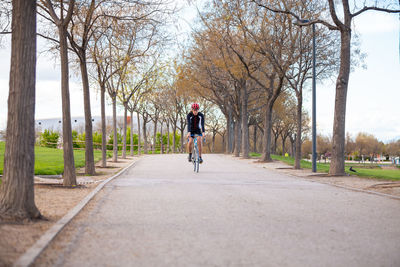 Man riding bicycle on road amidst bare trees