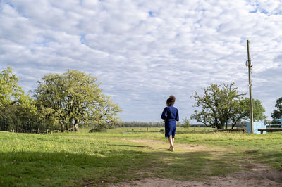 Rear view of man walking on field against sky