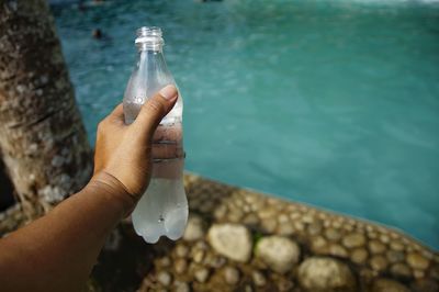 Midsection of person holding bottle in water