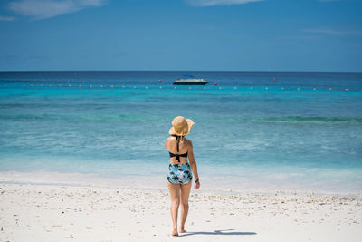 Rear view of woman wearing hat on beach against sky