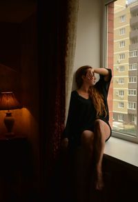 Young woman sitting on window at home