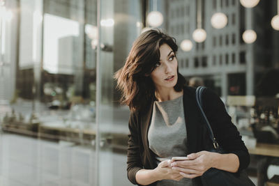 Woman looking away while using mobile phone by cafe