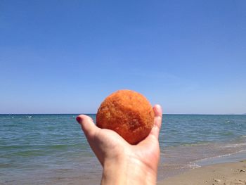 Close-up of hand holding apple against sea