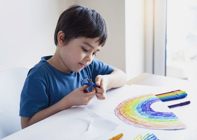 Boy holding scissors on table at home