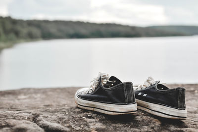 Close-up of shoes on rock against lake