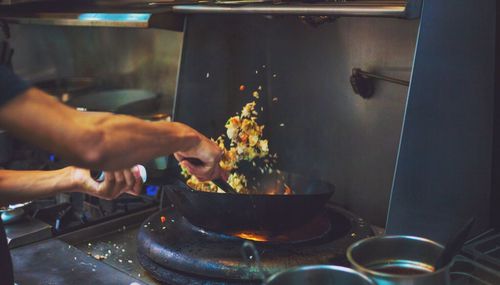 Cropped hand of chef cooking food on stove