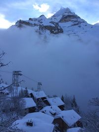 Snow covered houses by mountain against sky