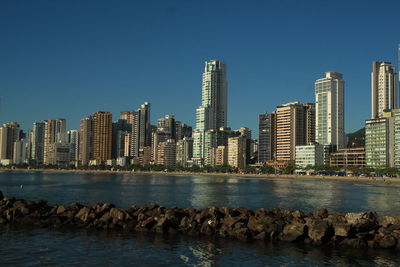 Sea by cityscape against clear blue sky