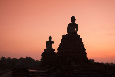 Low angle view of silhouette buddha statues against sky during sunset