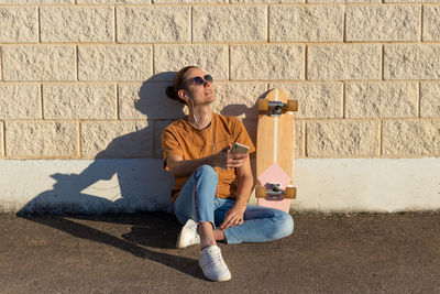 Relaxed young skate man sitting smiling and happy enjoying  wheather with his skateboard leaning