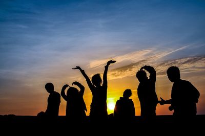 Silhouette friends standing against sky during sunset