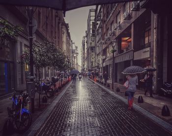 Rear view of people on street amidst buildings during rainy season