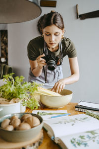 Food stylist photographing vegetable bowl using digital camera in studio