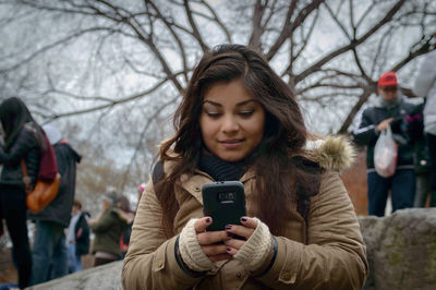 Young woman using mobile phone against sky