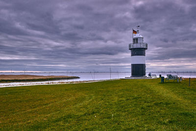 Lighthouse on field by sea against sky