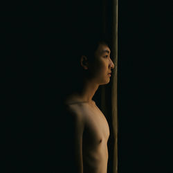 Side view of shirtless young woman against black background