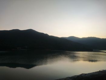 Scenic view of lake by silhouette mountains against clear sky