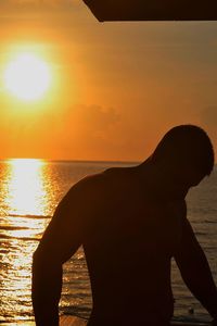 Silhouette man standing by sea against orange sky