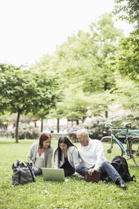 Business colleagues using laptop while relaxing on grass at park