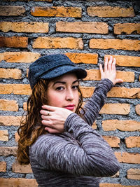 Portrait of confident young woman standing against brick wall