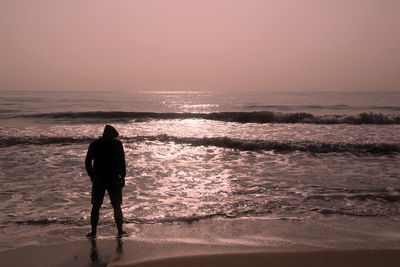 Rear view of man looking at sea against sky during sunset