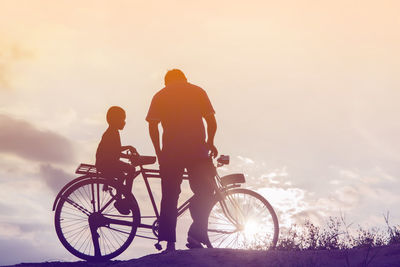 People riding bicycle against sky during sunset