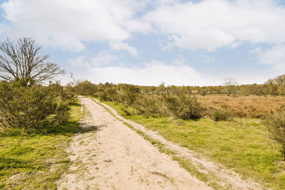 Dirt road amidst field against sky