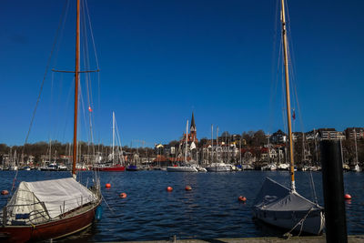 Sailboats moored in river against clear blue sky on sunny day at flensburg