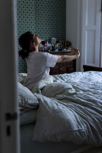 Young woman stretching arms sitting on bed at home