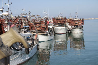 Fishing boats moored at harbor against clear sky