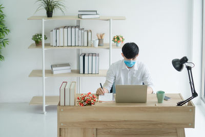 Rear view of man using mobile phone while sitting on table