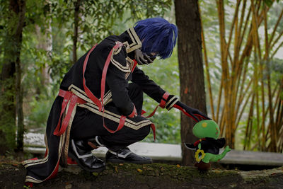 Rear view of man holding skateboard on land in forest