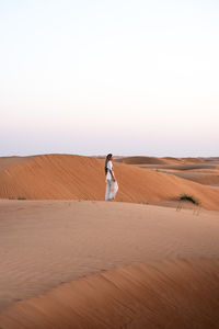 Rear view of woman walking at desert against clear sky
